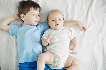 Children lie on the bed next to the newborn baby, little sister.