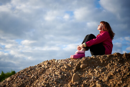 Photo of a caucasian woman in a jacket outdoors on a background of dreaming sky while sitting on the sand