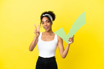 Young african american woman isolated on yellow background holding a check icon and celebrating a victory