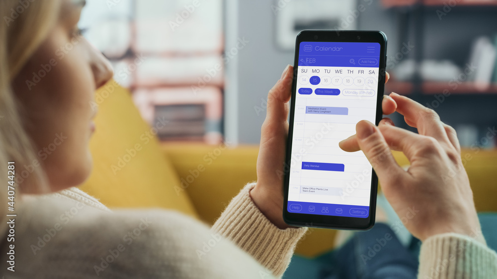 Aufkleber Beautiful Authentic Female Using a Smartphone with Calendar Application at Home Living Room while Lying on a Couch Sofa. She's Making Plans and Checking Event Schedule for a Day.