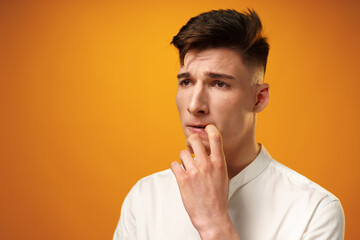 Frustrated and nervous young man biting nail against yellow background