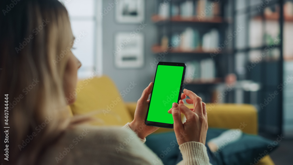 Aufkleber Beautiful Authentic Female Using a Smartphone with Green Screen Mock Up Display at Home Living Room while Lying on a Couch Sofa. She's Browsing the Internet and Checking Videos on Social Networks.