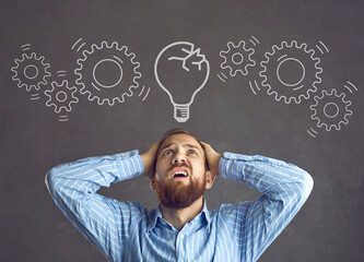 Stressed man looking at cracked light bulb and broken chain of gears. Corporate manager or...