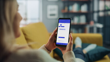 Beautiful Authentic Female Using a Smartphone with Calendar Application at Home Living Room while Lying on a Couch Sofa. She's Making Plans and Checking Event Schedule for a Day.