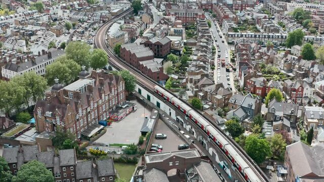 Cinematic drone follow shot of district line train winding through residential London Putney bridge