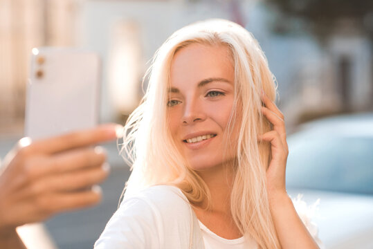 Happy Beautiful Girl 20-24 Year Old Making Selfie With Phone Over City Background Closeup. Looking At Telephone Have Video Call With Friends. Happiness.