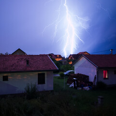 Thunderstorm above rooftops with lightning, extreme weather conditions during night, discharge of...