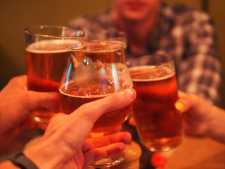 A group of friends drinking beer in a bar, close-up beer glasses toast