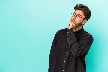 Young caucasian man isolated on blue background relaxed thinking about something looking at a copy space.