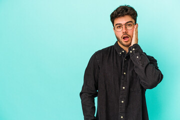 Young caucasian man isolated on blue background shouts loud, keeps eyes opened and hands tense.