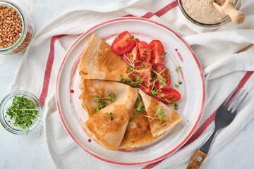 Stack of gluten free buckwheat flour crepes pancakes with cherry tomatoes and arugula microgreens on white plate, homemade healthy baking for breakfast. Mock up. Copy space.