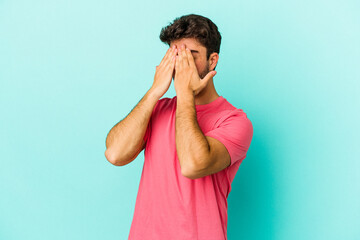 Young caucasian man isolated on blue background afraid covering eyes with hands.