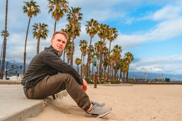 A man sits on a boardwalk along palm trees in Santa Barbara, California