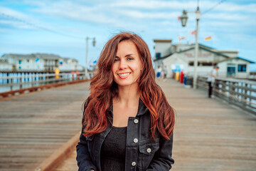 Cute smiling woman walks on a pier in Santa Barbara, California, USA - obrazy, fototapety, plakaty