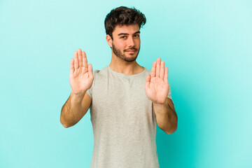 Young caucasian man isolated on blue background standing with outstretched hand showing stop sign,...