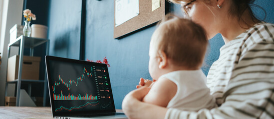 Fototapeta na wymiar Handsome woman with her cute baby investing in world stock market, using her laptop and online trading soft, working from home