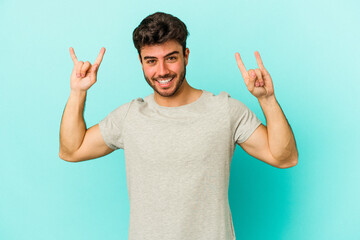 Fototapeta premium Young caucasian man isolated on blue background showing a horns gesture as a revolution concept.