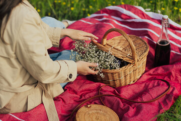 Woman sitting on the red blanket on the nature and touching the white flowers from picnic basket.