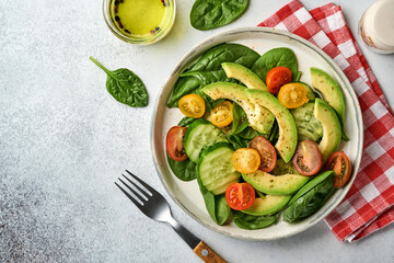 Avocado, red, yellow, black cherry tomato, spinach and cucumber fresh salad with spices pepper and olive oil in grey bowl on grey slate, stone or concrete background. Healthy food concept. Top view.