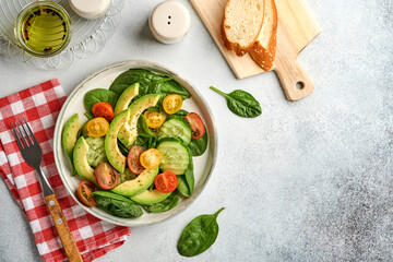 Avocado, red, yellow, black cherry tomato, spinach and cucumber fresh salad with spices pepper and olive oil in grey bowl on grey slate, stone or concrete background. Healthy food concept. Top view.