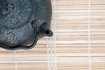Obraz premium Vintage, black metal Japanese tea pot on a reed pad with a lot of free space. Minimalistic tea ceremony concept.