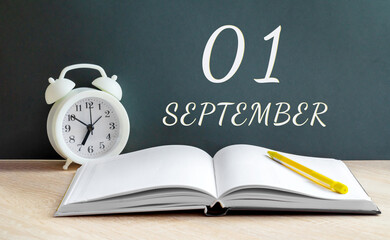 september 01. 01-th day of the month, calendar date.A white alarm clock, an open notebook with blank pages, and a yellow pencil lie on the table.Autumn month, day of the year concept