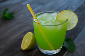 green drink or cocktail in a glass with a slice of lime and mint on a dark wooden background