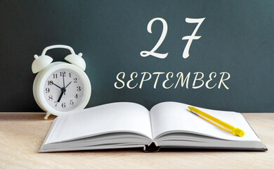 september 27. 27-th day of the month, calendar date.A white alarm clock, an open notebook with blank pages, and a yellow pencil lie on the table.Autumn month, day of the year concept