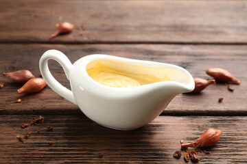 Tasty sauce in gravy boat, small onion bulbs and spice on wooden table