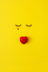 Feel sad about love. Artificial eyelashes with a red heart at the place of the lips and a tear in...