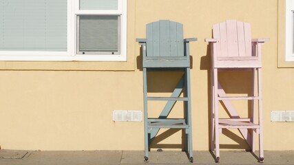 Two vintage wooden lifeguard chairs by yellow wall, California USA. Empty life guard retro high...