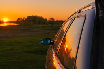 Close-up of a gray car with an open trunk on a blurry background of sunset and river, copy space
