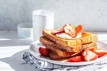 A stack of French toast with strawberries, yogurt and maple syrup. Breakfast concept.