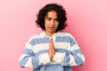Young curly latin woman isolated on pink background praying, showing devotion, religious person looking for divine inspiration.