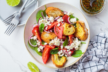 Italian salad with tomatoes, feta cheese and grilled ciabatta, marble background.