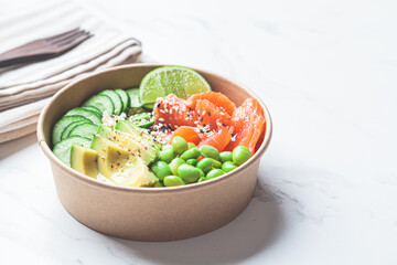 Poke bowl with rice, salmon, edamame beans, cucumber and avocado in reusable cardboard bowl. Hawaiian food. Zero Waste concept.