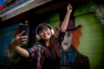 Young smiling woman outdoors. Beautiful woman listening to music while walking through the city.
