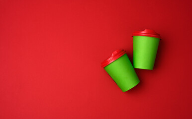 two green paper cups with a plastic lid on a red background, top view
