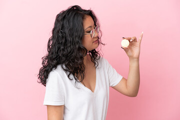 Young asian woman holding a Bitcoin isolated on pink background looking to the side