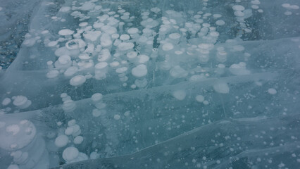 Turquoise ice. Close-up. Full frame. Cracks are visible on the smooth surface. Columns of frozen methane gas bubbles go into the depths. Lake Baikal