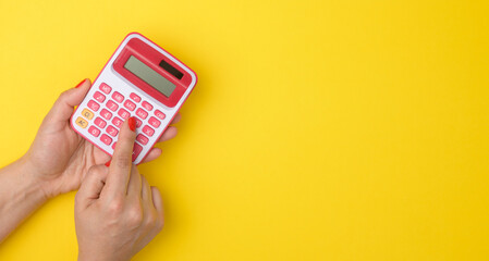 female hand holding a pink calculator on a yellow background, copy space