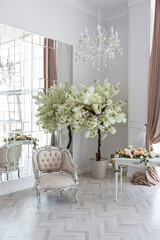 luxurious bright spacious guest room with beautiful chic furniture a huge floor-to-ceiling window in a royal style is decorated with green plants, white walls with stucco and a fireplace