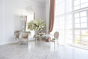 luxurious bright spacious guest room with beautiful chic furniture a huge floor-to-ceiling window in a royal style is decorated with green plants, white walls with stucco and a fireplace