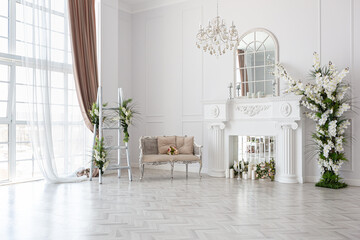 luxurious bright spacious guest room with beautiful chic furniture a huge floor-to-ceiling window in a royal style is decorated with green plants, white walls with stucco and a fireplace - obrazy, fototapety, plakaty