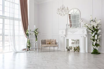 Fotobehang luxurious bright spacious guest room with beautiful chic furniture a huge floor-to-ceiling window in a royal style is decorated with green plants, white walls with stucco and a fireplace © 4595886