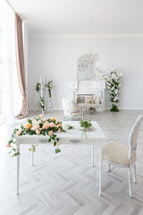 luxurious bright spacious guest room with beautiful chic furniture a huge floor-to-ceiling window in a royal style is decorated with green plants, white walls with stucco and a fireplace