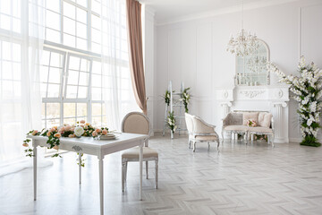 luxurious bright spacious guest room with beautiful chic furniture a huge floor-to-ceiling window in a royal style is decorated with green plants, white walls with stucco and a fireplace