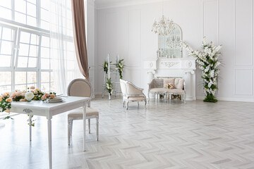 luxurious bright spacious guest room with beautiful chic furniture a huge floor-to-ceiling window in a royal style is decorated with green plants, white walls with stucco and a fireplace