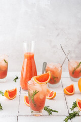 Cold refreshing grapefruit smoothie with rosemary and ice in glasses, grapefruit wedges and rosemary sprigs on the table, home party