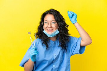 Young asian dentist holding tools over isolated background celebrating a victory
